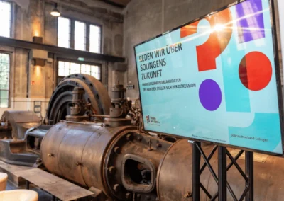 Großer Bildschirm und industrielle Kulisse während eines Presseevents und Interviews in der Alten Maschinenhalle Solingen.