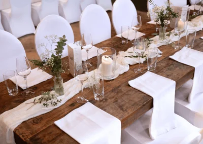 Lange Hochzeitstafel mit Holzoberfläche, weißen Stühlen, Kerzen und floraler Tischdekoration in der Alten Maschinenhalle Solingen