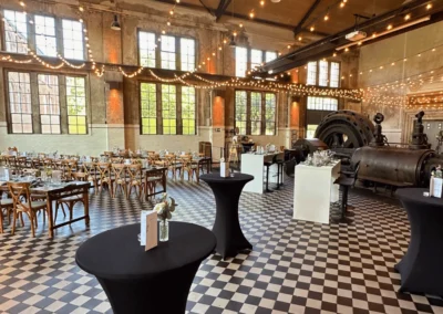Weitläufiger Hallenraum mit Stehtischen, Lichterketten und historischer Dampfmaschine