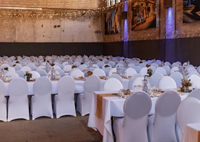 Weitläufige Ansicht der Alten Kesselhalle Solingen mit Reihen von festlich gedeckten Tischen, weißen Stuhlhussen und stimmungsvollen Lichterketten unter der Decke.