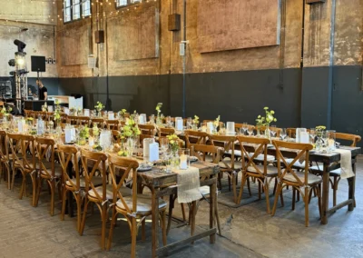 Lange Holztische mit Holzstühlen und Lichterketten für ein Festessen in der Alten Kesselhalle.